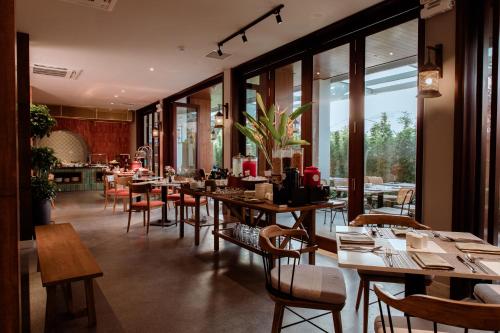 Un restaurante con mesas y sillas de madera y ventanas. en Little Gem. An Eco-Friendly Boutique Hotel & Spa, en Hoi An