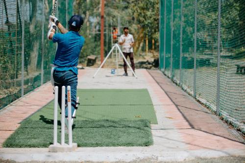 a man swinging a bat in a batting cage at Daksh Eden Greenz -A Luxury Resort in Sasan Gir in Sasan Gir