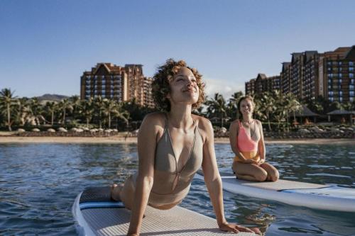 two women in bathing suits sitting on surfboards in the water at Aulani, Disney Vacation Club Villas in Kapolei