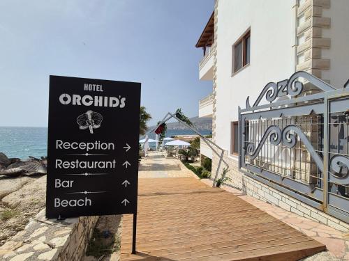 ein Schild vor einem Gebäude neben dem Meer in der Unterkunft ORCHIDS Hotel in Sarandë