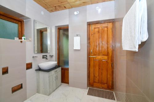 Thiksay Organic Resort في Ranbirpura: حمام وباب خشبي ومغسلة