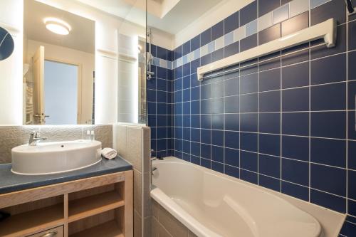 Pierre & Vacances Premium Résidence de la Plage في لو كروتوي: حمام من البلاط الأزرق مع حوض استحمام وحوض استحمام