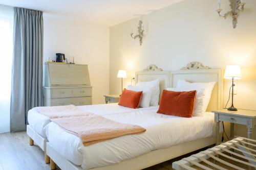 - une chambre avec un grand lit blanc et des oreillers orange dans l'établissement Hôtel Le Martray, à Ars-en-Ré