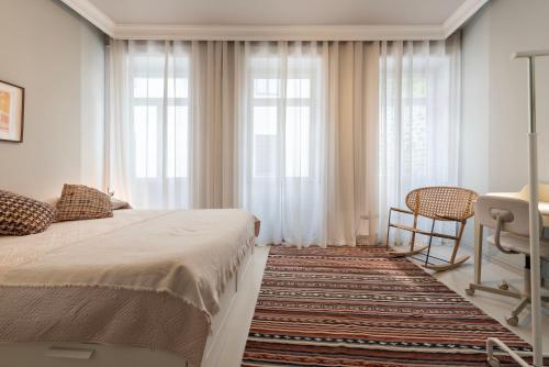 a bedroom with a bed and a chair and windows at Marias River Apartment in Porto