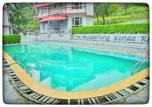 a swimming pool with blue water in front of a building at Whispering Winds Resort in Dharamshala