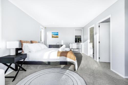 a white bedroom with a bed and a table at Stylish warm house in north Hamilton in Hamilton