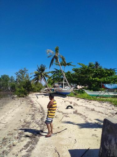 a young boy standing on a beach with a boat at Rose Cabins Bohol in Loon