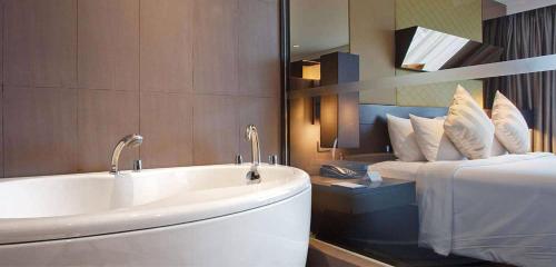 a bathroom with a tub and a bed with a mirror at Golden Tulip Mandison Suites in Bangkok