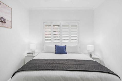 a white bedroom with a large bed with a blue pillow at Marlo's Escape - A Generous Haven for Couples in Wollongong