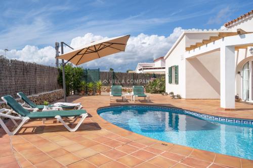 a swimming pool with two chairs and an umbrella at Villa Isabel in Cala En Porter in Cala'n Porter