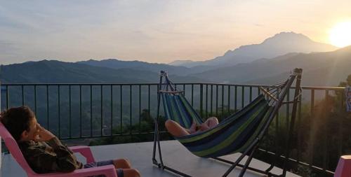 a man sitting in a hammock on a balcony overlooking mountains at Hawun Valley Kiulu in Tamparuli