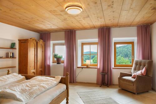 Schlafzimmer mit einem Bett, einem Stuhl und Fenstern in der Unterkunft Landhaus am Eselhof Daxstein in Schöllnach