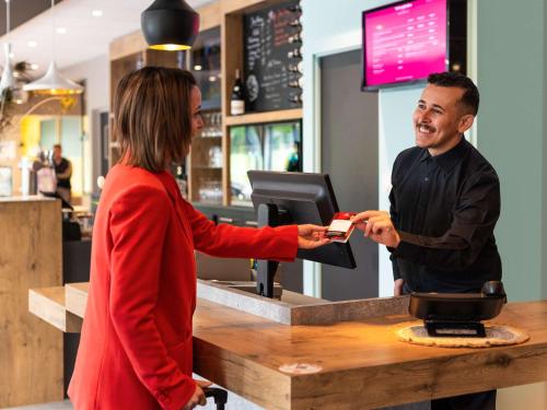 Une femme qui donne à un homme une carte de crédit à un comptoir dans l'établissement ibis Nuits Saint Georges, à Nuits-Saint-Georges