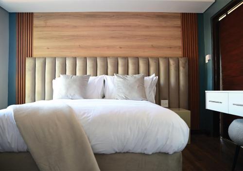 a bedroom with a large white bed with a wooden headboard at Omni The Pillar Boutique Hotel in Bloemfontein
