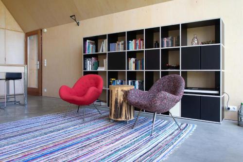 two red chairs in a living room with a book shelf at Urlaub in Designer-Ferienwohnung, die zusätzlich mit traditionellem Weinkeller und hochwertiger Einrichtung überzeugt in Sausal