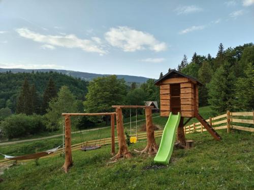 a playground with a wooden house and a green slide at Chata Terasa Kubinska in Dolný Kubín
