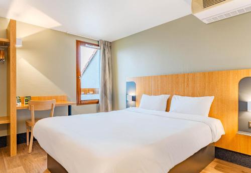 a large white bed in a room with a window at B&B HOTEL Poitiers 3 Futuroscope in Chasseneuil-du-Poitou