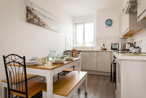 a white kitchen with a wooden table and a dining room at Quayside View - Luxury Apartment on Paignton Harbour in Paignton