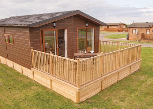 a wooden cabin with a large deck in the grass at Holderness Country Park in Tunstall
