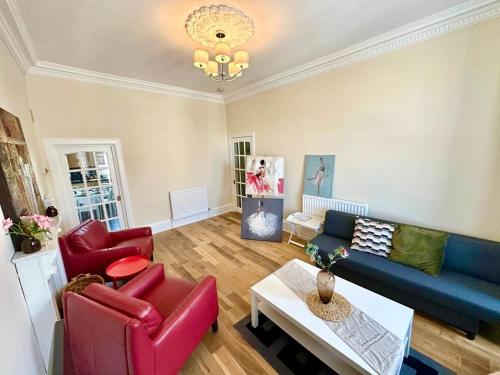 Dumbarton cosy home, Loch Lomond في دمبارتون: غرفة معيشة مع أريكة زرقاء وكراسي حمراء