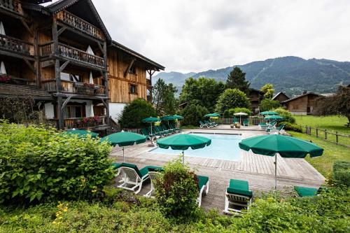 une piscine avec des parasols verts devant un immeuble dans l'établissement Residence Hôtelière La Renardiere, à Samoëns