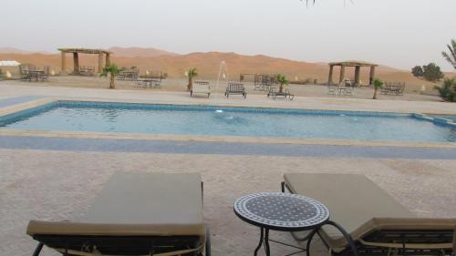 a swimming pool with tables and chairs next to it at SANDSTAR PALACE in Merzouga