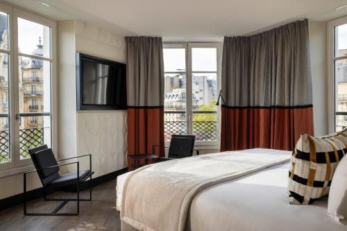 a bedroom with a bed and two chairs and windows at Hôtel Raspail Montparnasse in Paris