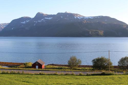 un granero rojo a un lado de un lago con una montaña en Slåtteng, en Svensby