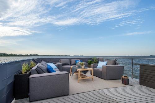 a deck with couches and a table on the water at Hausboot Seeadler Stralsund in Stralsund