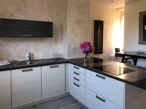 - une cuisine avec des placards blancs, un évier et des fleurs violettes dans l'établissement la maison du centre, à Lannion