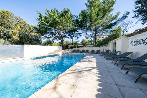 a swimming pool with chairs and trees in the background at Hôtel La Garrigue & Bar Piscine in Venasque