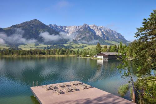 a view of a lake with a house and mountains at Hotel Das Walchsee in Walchsee