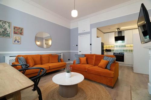 ロンドンにあるLamington Apartments - Hammersmithのリビングルーム(オレンジ色のソファ2台、テーブル付)