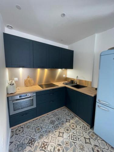 La cuisine est équipée de placards bleus, d'un évier et d'un réfrigérateur. dans l'établissement Maison de village, à Caux