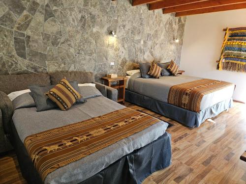 a bedroom with two beds and a stone wall at Lodge Quelana in San Pedro de Atacama