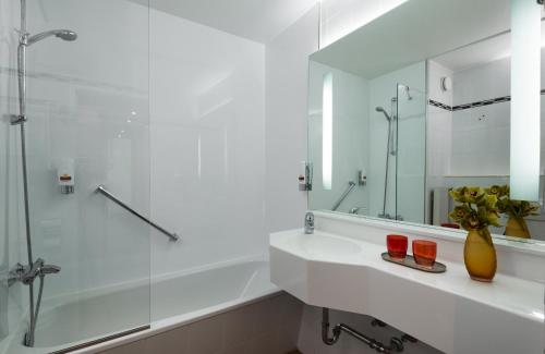 Baño blanco con lavabo y espejo en Leonardo Hotel Munich Arabellapark, en Múnich