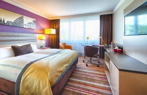 a hotel room with a bed and a desk at Leonardo Royal Hotel Köln - Am Stadtwald in Cologne
