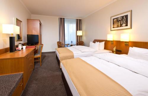 a hotel room with two beds and a desk at Leonardo Hotel Aachen in Aachen