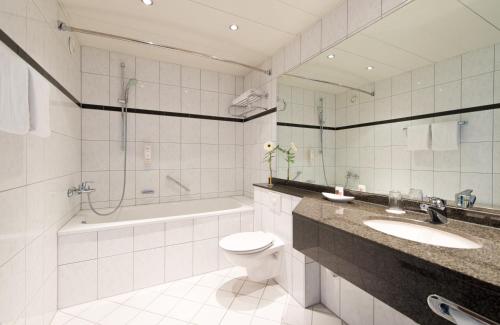 een badkamer met een toilet, een wastafel en een bad bij Leonardo Hotel Köln Bonn Airport in Keulen