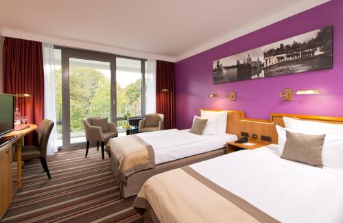 two beds in a hotel room with purple walls at Leonardo Hotel Hannover in Hannover