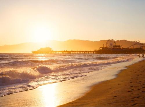 a beach with a pier in the water and the sun at Regent Santa Monica Beach in Los Angeles