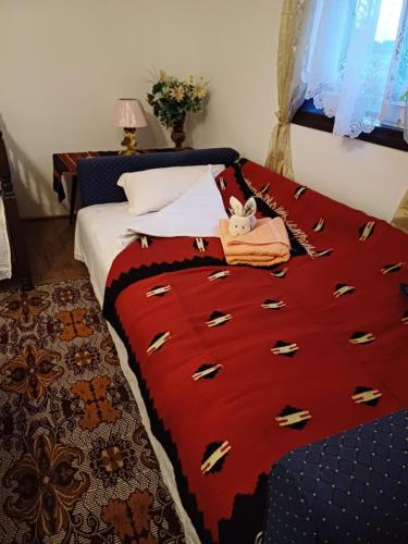 a bed with a red blanket with a stuffed animal on it at Seosko Domaćinstvo Jevtić in Ždraljica