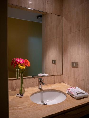 a bathroom sink with a vase of flowers and a mirror at Hotel Britania San Borja in Lima