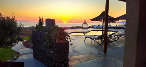 a sunset from a patio with a table and an umbrella at Thea Luxury Resort in Fira