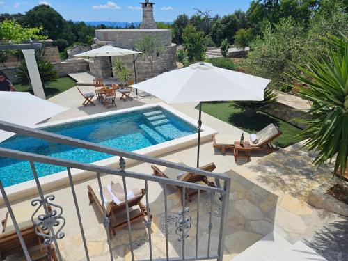 a swimming pool with an umbrella and chairs and a patio at Villa Žurnata in Bogomolje