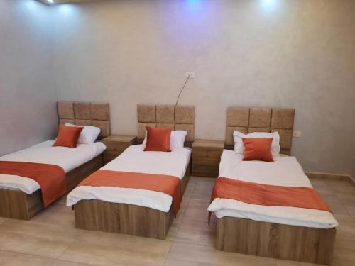 a room with three beds with orange and white sheets at Tala DeadSea Villa in Sowayma
