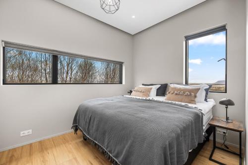 a white bedroom with a large bed and two windows at Spacious 4BR Summerhouse With Hot Tub in Reykholt