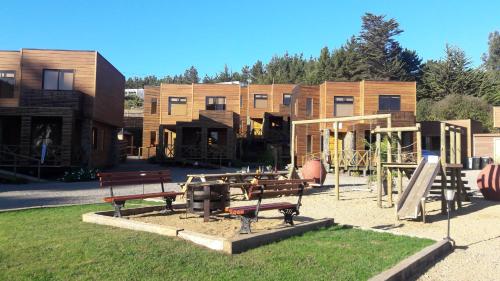a park with benches and a playground in front of buildings at Cabañas Rancho Pinares in Pichilemu