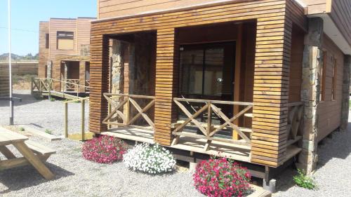 a small wooden cabin with flowers and a bench at Cabañas Rancho Pinares in Pichilemu