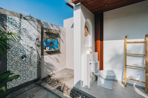 a bathroom with a toilet and a wall at Suga Estate - Rice Field View Villas in Ubud
